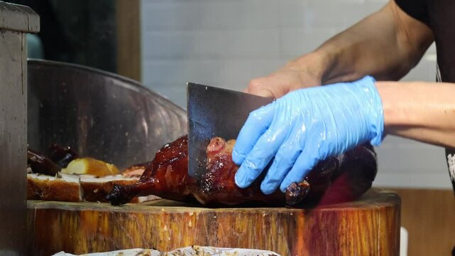 Close-up of a cooked roast goose being expertly sliced by a chef using a cleaver knife on a wooden board