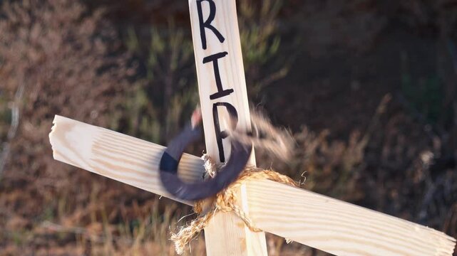 Close-up of fresh grave, hand hangs old horseshoe on rope on a wooden cross with the inscription rip Farewell to the deceased, amulet, talisman for memory, protection from evil spirits Burial rituals