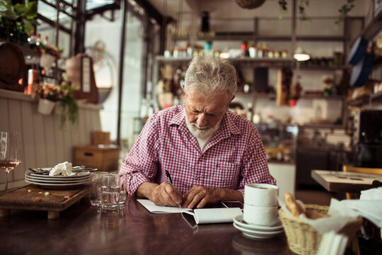 Senior male restaurant bistro owner doing expanses after shift