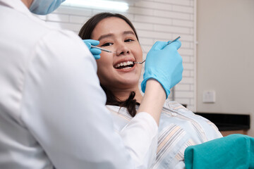 Asian male dentist examines beautiful young female patient's teeth stomatology in dental clinic, well-being hygiene checks, and professional orthodontic healthcare work in doctor's office hospital.