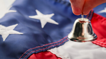person holding a small silver bell over united states flag. metaphor freedom ring abstract concept with red, white, and blue colors american flag patriotic theme full frame stars stripes background.