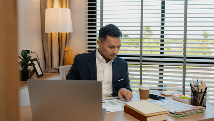 Fototapeta premium middle aged professional businessman wearing white shirt and suit happily smiling in office, a middle-aged, dark-haired businessman in a suit is happily working at his desk in the office