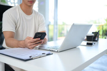 Young entrepreneur sitting at modern workplace and using mobile phone