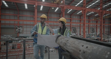 Fototapeta premium Metal sheet workers inspecting blueprint in factory setting. Collaborating on project planning and precision engineering, surrounded by machinery and equipment essential for manufacturing process. 