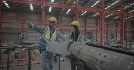 Fototapeta premium Metal sheet workers inspecting blueprint in factory setting. Collaborating on project planning and precision engineering, surrounded by machinery and equipment essential for manufacturing process. 
