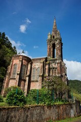 Fototapeta premium A gothic-style church with a tall spire set against a clear blue sky in a lush green landscape.