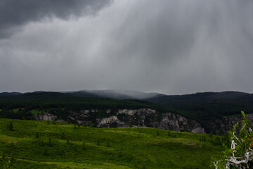 Dramatic view of Katu-Yaryk Pass in Altai with rugged cliffs, lush vegetation, and dark storm clouds rolling over the mountains. Nature, travel, and dramatic landscape photography