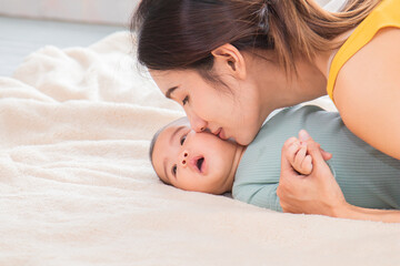 Asian beautiful young mother teases her newborn daughter and kissing cheek with love. Single mom...