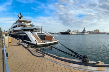 A sleek luxury yacht docked at a marina with several other yachts in the background. The scene...