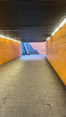 A quiet underground tunnel with bright lighting and an escalator leading up to the next level. The...