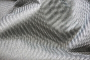 A close-up of a smooth, gray fabric with a tightly woven pattern. The material has a glossy finish...