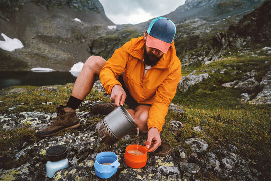 Man setting up backcountry kitchen to prepare dinner cooking camping meals using gas stove outdoor gear on picnic in mountains - travel solo hiking survival trip adventure vacations summer eco tourism