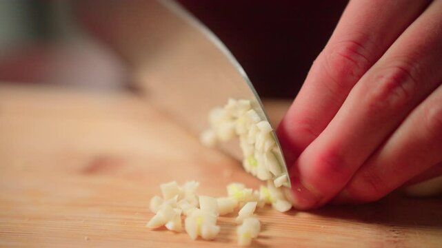 Woman cutting cloves of garlic by hand with a knife on a cutting board
