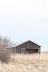 Obraz premium Rustic barn surrounded by dry grasses and soft clouds in a rural landscape