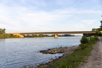 A wide view of a bridge spanning across a calm river, surrounded by lush green vegetation on both sides.