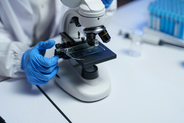 Close-up of gloved hands adjusting a microscope slide on a modern microscope in a medical...