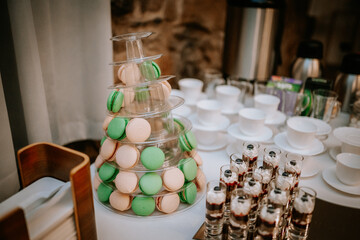 A dessert table with a macaron tower in pastel colors, small dessert shots, and cups arranged elegantly for a party or event.