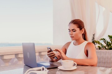 Fototapeta premium Woman coffee cafe laptop sea. Modern businessman in white uniform working on laptop in coffee shop. Woman sitting at a coffee shop with mobile phone drinking coffee.