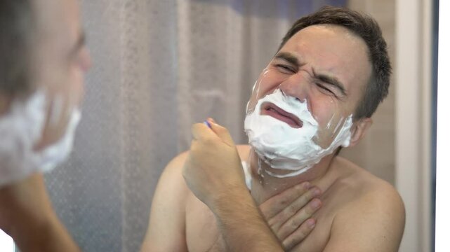 man shaves his face without cream or foam, experiencing pain and suffering. sad man shaves in front of a mirror in the morning. Unhealthy shaving of the face with skin irritation.