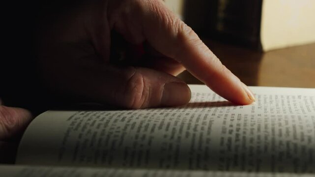 A person studying the dictionary. A finger in close-up slowly runs down the lines of words and letters in an open book