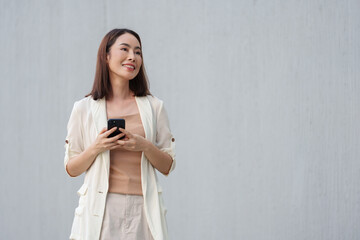 Young asian businesswoman is using a smartphone and looking away with a smile while standing...
