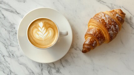 A cup of latte art coffee with a croissant on a marble surface