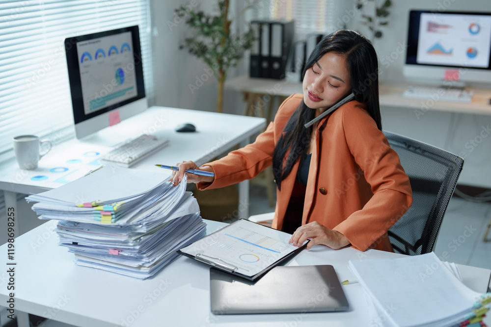 Poster young office worker talking on the phone while searching for a document in a large pile of paperwork