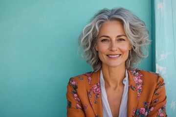 Happy woman with curly gray hair smiling against a turquoise background in a casual setting