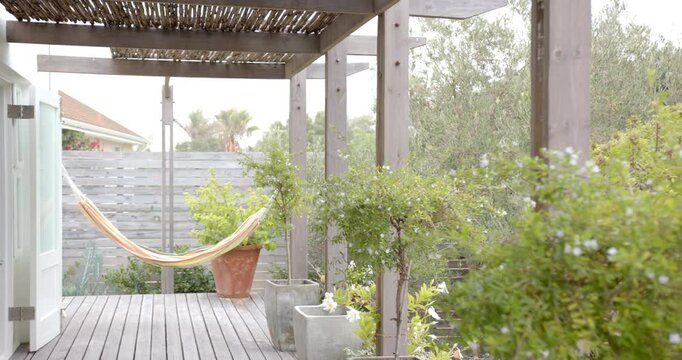 Empty hammock hanging on wooden deck in peaceful backyard garden, copy space