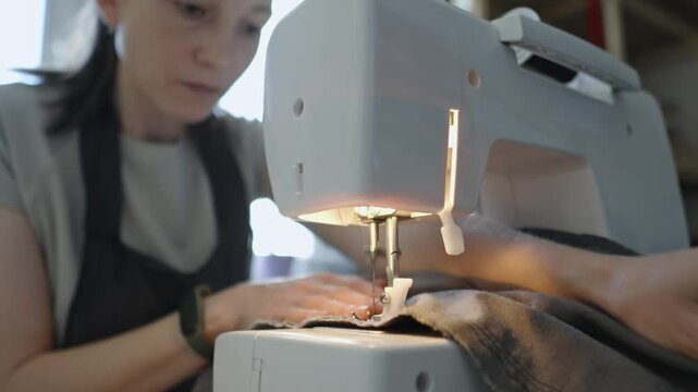 A female tailor is working on a sewing machine stitching fabric. Home sewing production