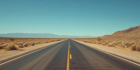 A straight road stretches through a vast desert landscape, leading towards distant mountains under a clear blue sky.