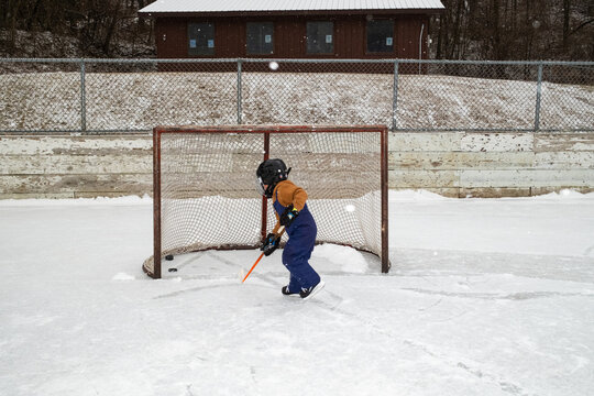 Child playing hockey on an outdoor snowy rink by a rustic fence