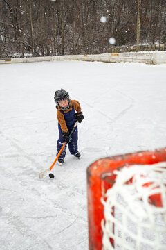 Child Playing Hockey on Outdoor Ice Rink with a Goal in View