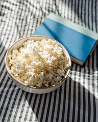 popcorn in ceramic bowl with a book on a striped cloth