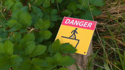 Danger warning sign saying informing passers by of falling down off on cliff