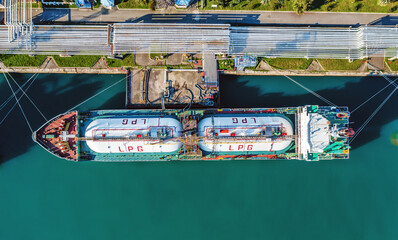 Top-down view of LPG tanker docked at industrial port terminal with visible pipelines for gas transfer. Symmetrical composition emphasizes maritime trade and infrastructure.