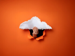 A hand emerges from a torn orange background, gesturing beneath a cloud-shaped hole.  The scene is surreal and minimalist.
