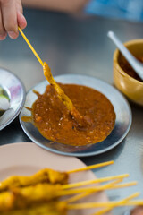 Eating satay pork marinated with yellow spices dip sweet peanut sauce at restaurant.