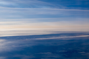 Dramatic contrail stretches across layered clouds in high altitude aerial view. Natural abstract pattern of aircraft vapour trail against deep blue sky and stratiform cloud formations