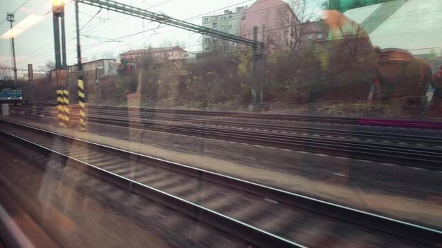 View from inside a train looking out on parallel tracks, with reflections of the interior and passengers visible on the window