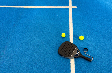 Black professional paddle tennis racket and ball with natural lighting on blue background....