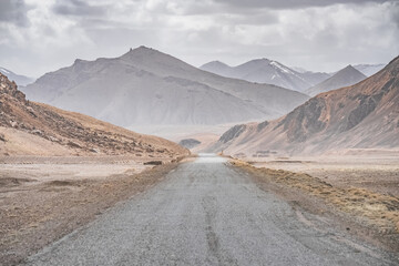 Asphalt road of the Pamir Highway in the valley of the Tien Shan Mountains in Tajikistan in the Pamirs, landscape in the high desert mountains for background, the road goes into the distance