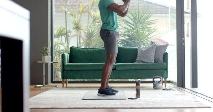 Exercising at home, man doing squats on yoga mat with kettlebell nearby