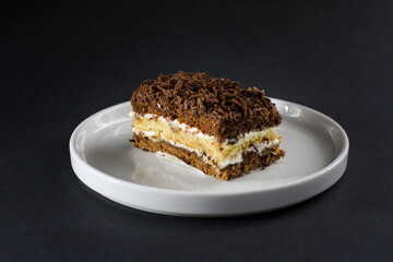 Primer plano de trozo de torta de chocolate rellena de glaseado y por encima chocolate rayado, parecido a tiramisu