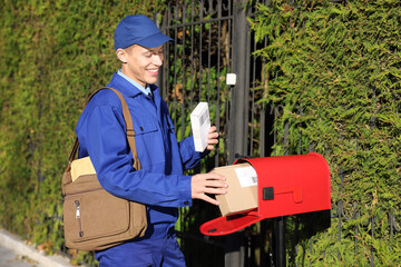 Postman putting parcel into mail box outdoors