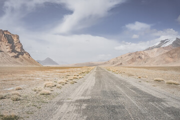 Asphalt road of the Pamir Highway in the valley of the Tien Shan Mountains in Tajikistan in the Pamirs, landscape in the high desert mountains for background, the road goes into the distance