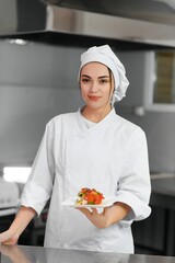 young beautiful smiling woman chef wearing in white suit at kitchen. Blurred background