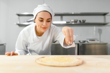 Female chef sprinkles cheese on pizza, restaurant kitchen