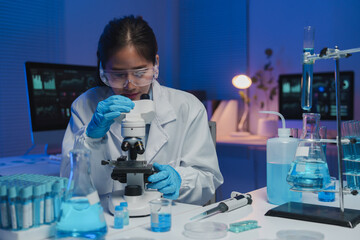 Young female scientist wearing lab coat and gloves using microscope in modern laboratory, conducting research, analyzing samples, and developing new medicine or chemical substance