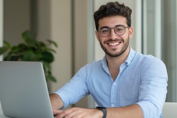 A man is sitting at a table with a laptop in front of him. He is smiling and he is happy